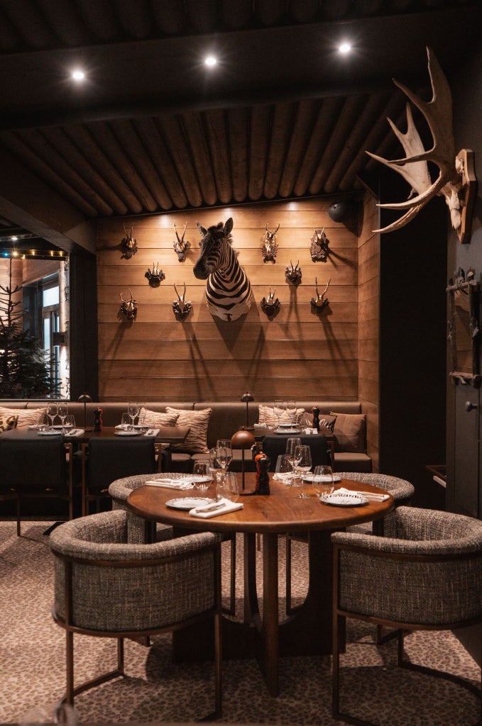 Elegant lodge-style hotel with wood-paneled facade, nestled in French alpine landscape, featuring rustic luxury and snow-capped mountain backdrop