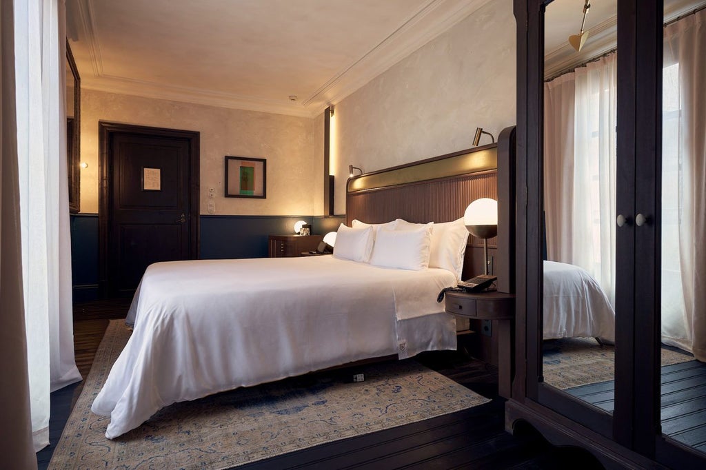 Elegant junior suite with soft neutral tones, antique wooden furniture, plush bedding, and ornate architectural details in historic Spanish boutique hotel