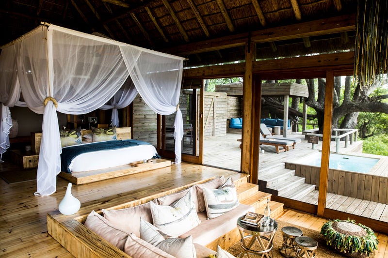 Modern luxury safari lodge with thatched pavilions elevated on wooden decks overlooking pristine African savanna at sunset