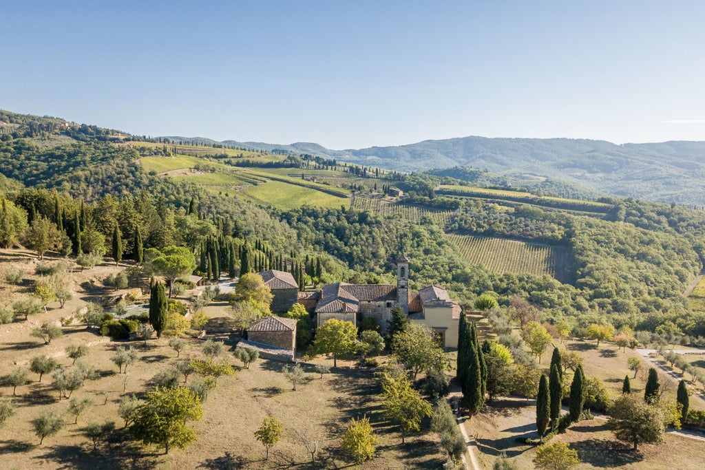 Historic stone villa with terracotta roof nestled in rolling Tuscan hills, featuring elegant arched windows and manicured cypress gardens