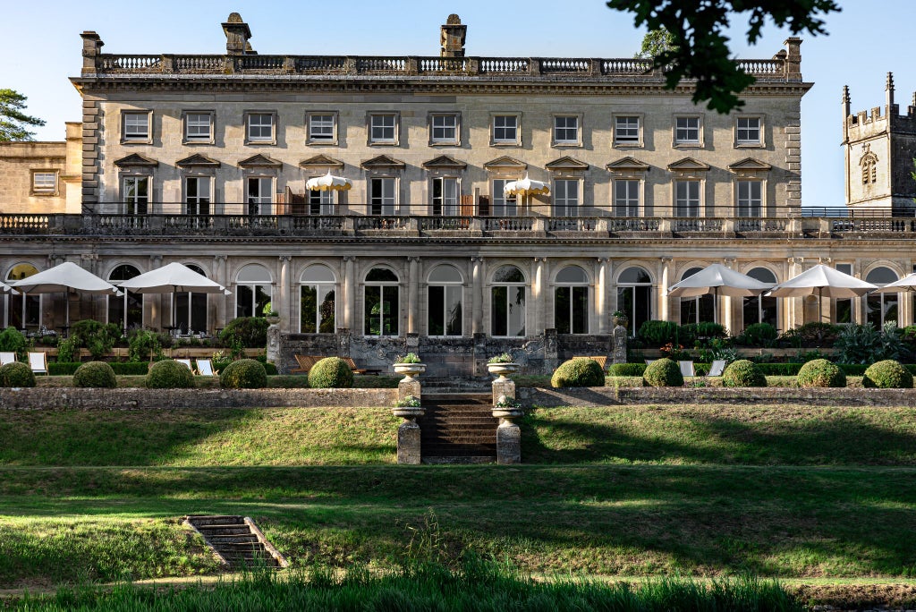 Luxurious countryside hotel with modern architectural design, stone facade, manicured gardens, and contemporary glass elements nestled in lush green landscape