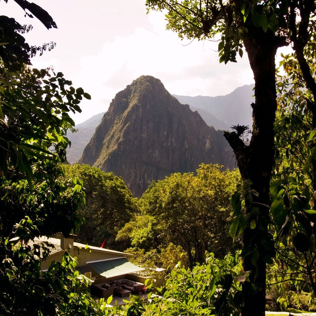 Luxury mountaintop hotel nestled below Machu Picchu's ancient ruins, featuring stone walls, lush gardens, and panoramic Andes views