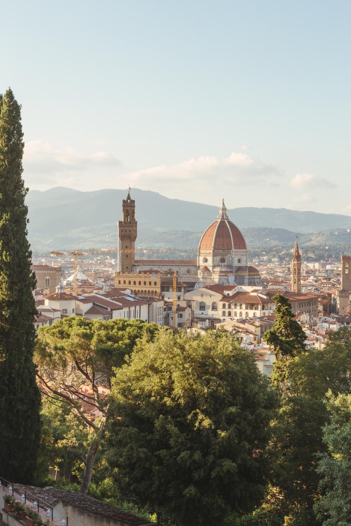 Florence's iconic Duomo cathedral rises above terracotta rooftops at sunset, with cypress trees dotting the romantic Tuscan cityscape