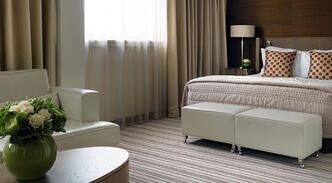 Elegant deluxe hotel room with plush king bed, sophisticated neutral decor, large windows overlooking urban scenery in central United Kingdom accommodation