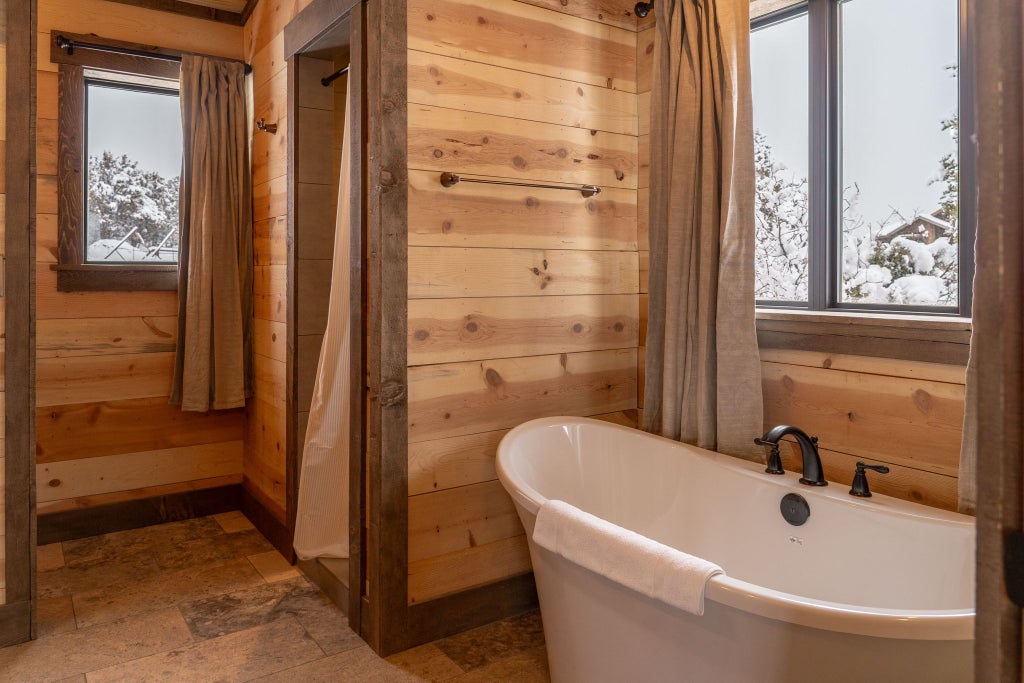 Rustic wooden lodge room with plush king bed, panoramic mountain views, warm earth tones, and elegant southwestern-inspired decor at scenic wilderness retreat