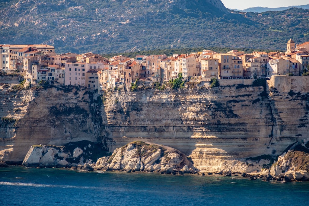 Sandy Mediterranean beach with turquoise waters against dramatic rocky cliffs, luxury boats docked in Corsica's pristine natural harbor