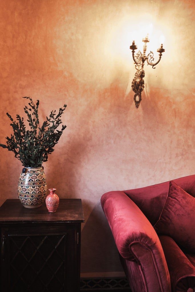 Traditional Moroccan riad with ornate tiles, flowing fountain and lush courtyard garden surrounded by whitewashed archways and balconies