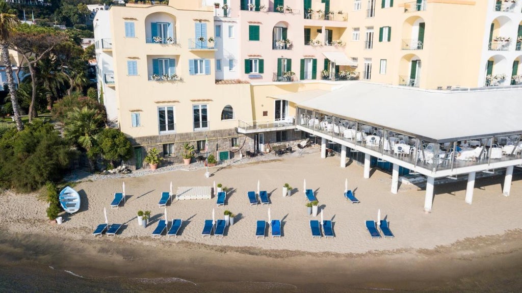 Elegant Italian seaside hotel with white Mediterranean architecture, palm trees, and a panoramic ocean-view terrace overlooking Ischia's coastline