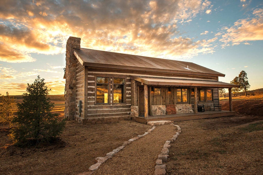 Rustic luxury lodge nestled in mountains, featuring wooden beams, stone fireplace, cathedral ceiling, and panoramic canyon views