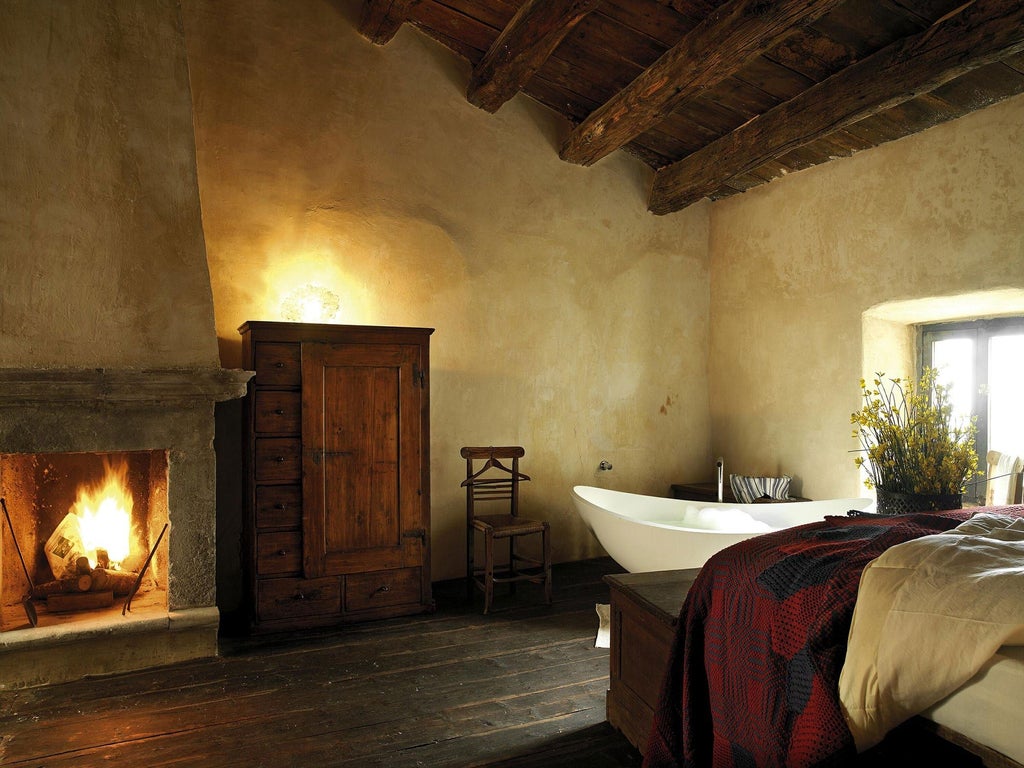 Rustic stone-walled hotel room with antique wooden bed, arched window overlooking Italian village bell tower, soft warm lighting