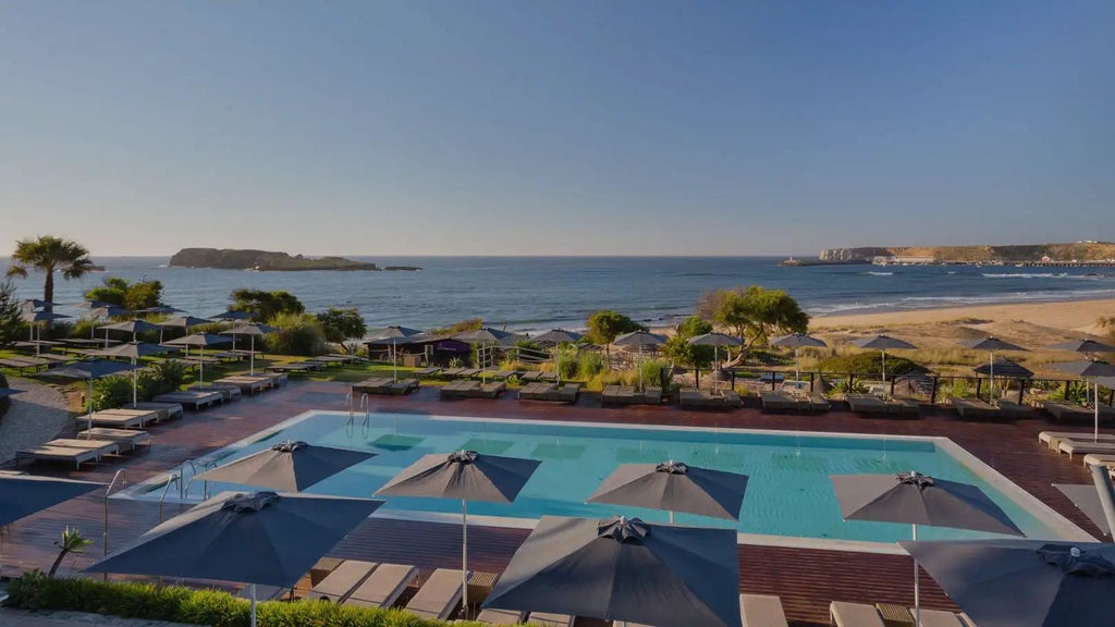 Luxurious beachfront resort in Sagres, Portugal, with modern white buildings, azure pool, and golden sandy beach with Atlantic Ocean backdrop