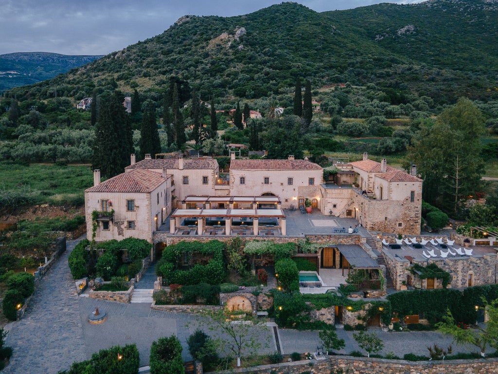 Historic stone-built luxury hotel with arched windows and balconies nestled among lush gardens overlooking the Aegean Sea and mountains