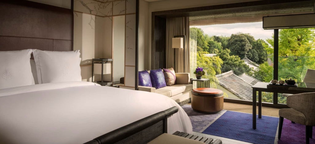 Elegant hotel room with floor-to-ceiling windows overlooking Kyoto, featuring tatami seating area and minimalist Japanese decor