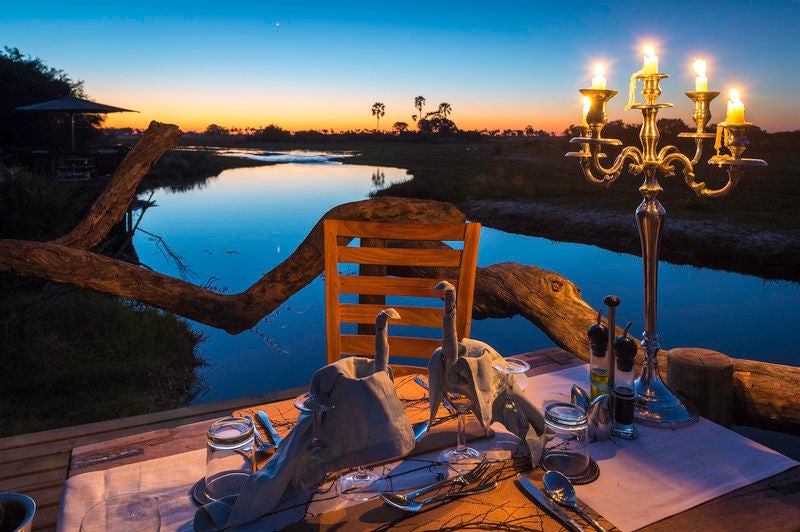 Luxurious elevated safari lodge with thatched roof and wooden deck overlooking vast floodplains and acacia trees in Botswana