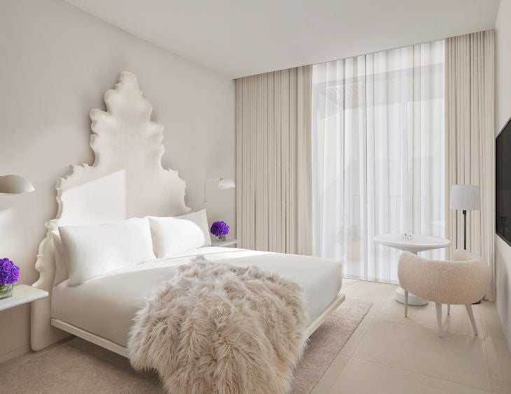 Elegant hotel room featuring a king bed with white linens, modern wood furnishings, floor-to-ceiling windows and private balcony with city views