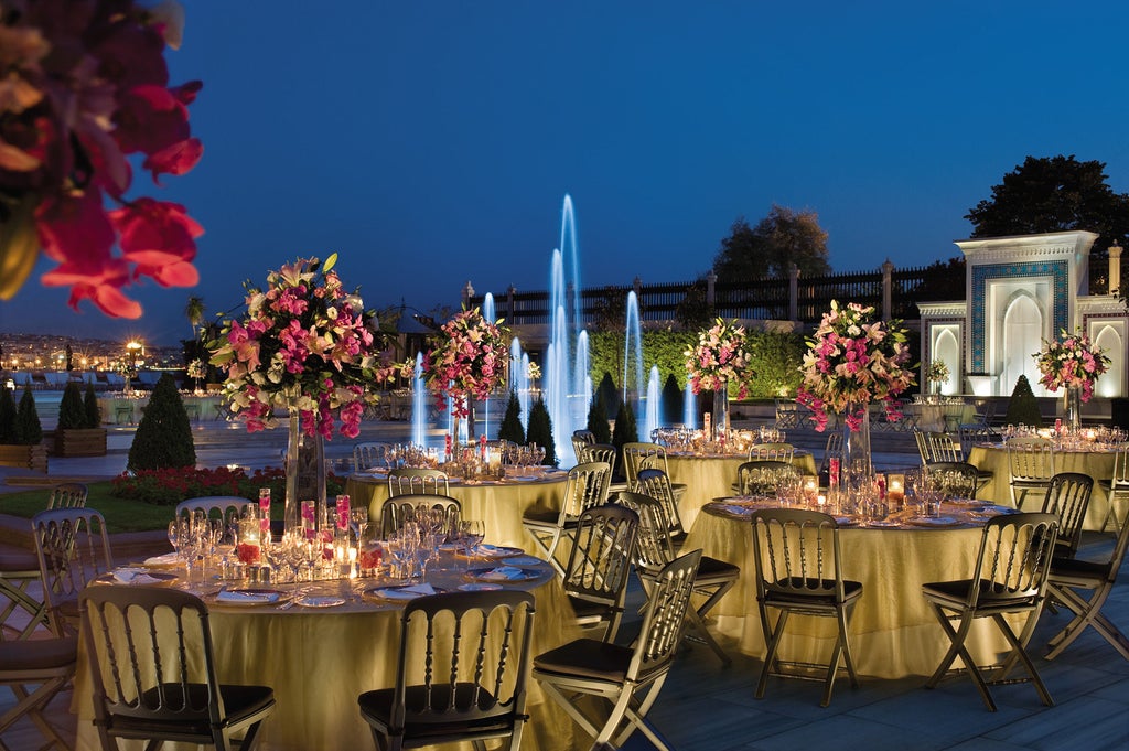 Opulent Ottoman palace-turned-hotel with grand white facade overlooking Bosphorus strait, featuring manicured gardens and waterfront terrace