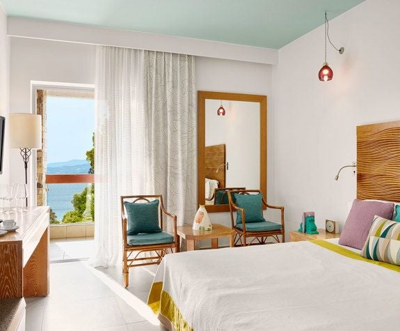 Elegant sea-view double room with crisp white linens, modern minimalist design, and panoramic azure Aegean Sea backdrop at Eagles Palace resort, Greece.