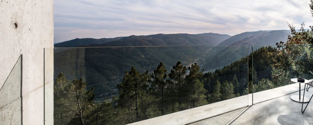 Luxurious hotel room with panoramic mountain view, modern design featuring clean lines, warm wood tones, and expansive glass windows overlooking scenic landscape in Portugal