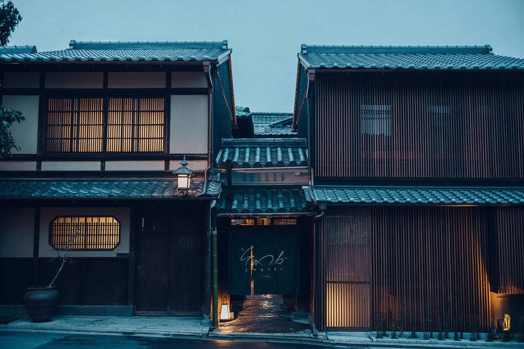 Traditional Japanese ryokan with wooden facade, stone pathway, lanterns, and immaculate zen garden featuring manicured bonsai trees.