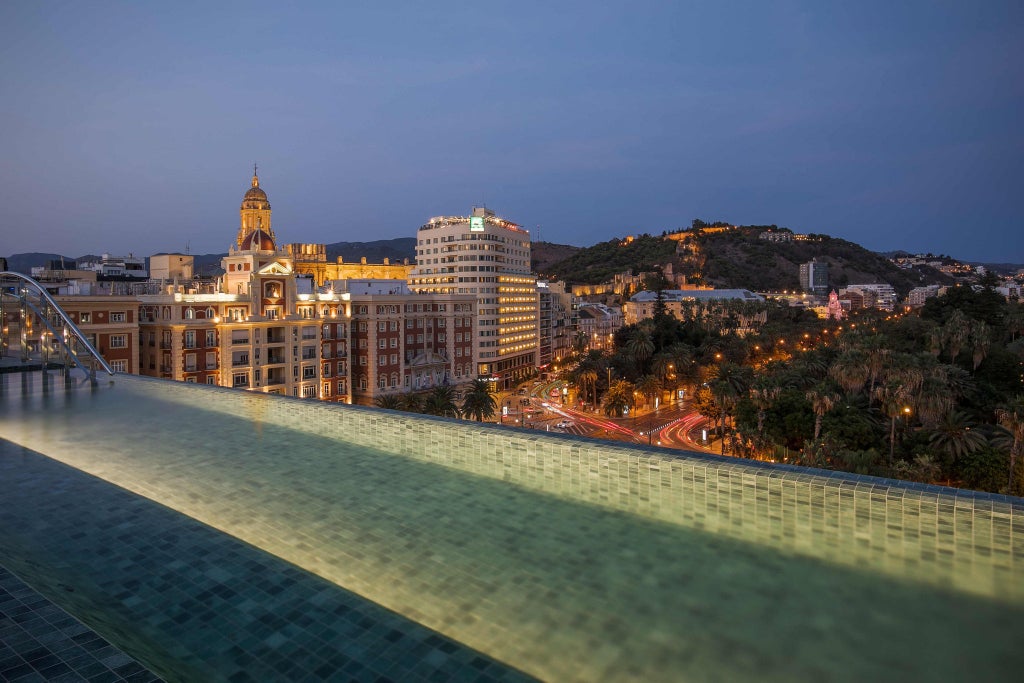 Trendy rooftop bar with infinity pool at Only You Malaga hotel featuring modern loungers, city views and ambient lighting at sunset