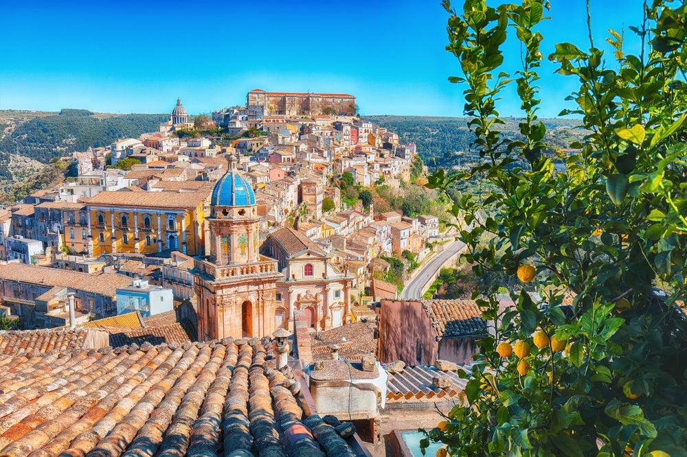 Elegant baroque architecture of Noto, Sicily, with sun-drenched limestone buildings, ornate balconies, and historic cathedral gleaming against azure sky