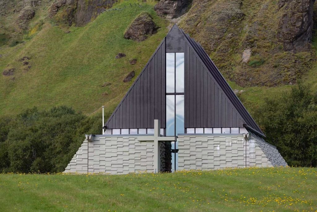 Elegant Iceland hotel with pitched roofs and modern glass entrance set against snowy mountain backdrop and dramatic cloudy sky