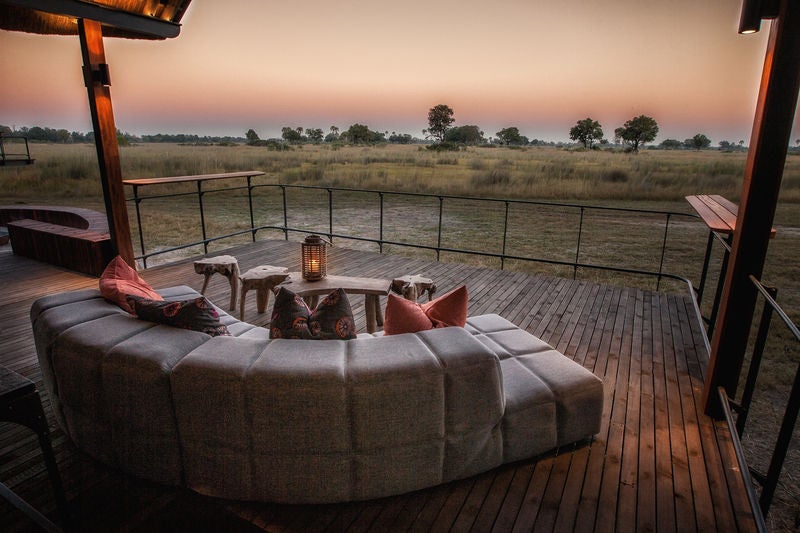 Luxurious safari lodge overlooking floodplains, featuring elevated wooden walkways and thatched-roof villas nestled among acacia trees