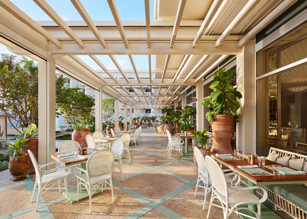 Oceanfront luxury hotel with white Mediterranean-style facade, swaying palm trees, and elegant pool area overlooking private beach at sunset