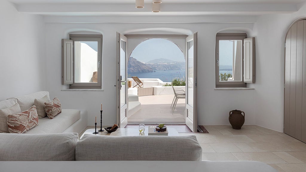 Luxurious white-themed Grand Two Bedroom Suite overlooking deep blue Aegean Sea, featuring minimalist design and private balcony with stunning Santorini landscape view