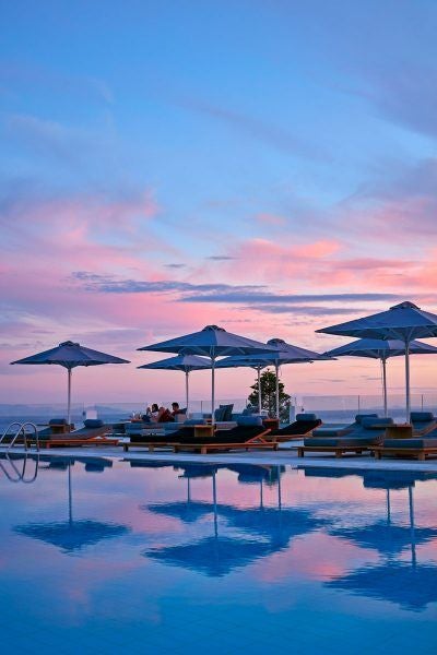 Luxurious white-washed Cycladic hotel with infinity pool overlooking azure Aegean Sea, blending modern design with traditional Greek island architecture