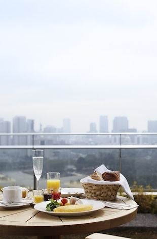 Elegant hotel room with floor-to-ceiling windows, modern furnishings, and a private balcony overlooking Wadakura Fountain Park in Tokyo, Japan