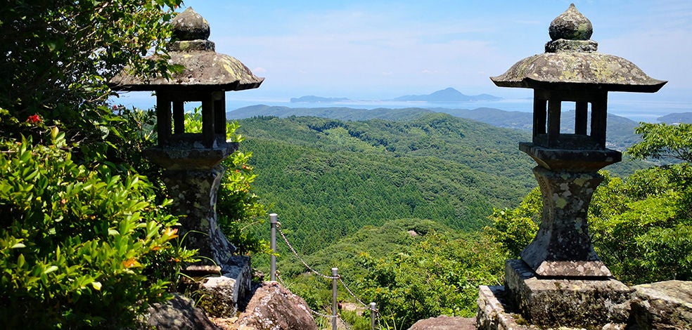 Lush green terraced landscapes of Kunisaki Peninsula, with traditional stone Buddhist statues nestled among misty mountain slopes and verdant rice paddies in rural Japan