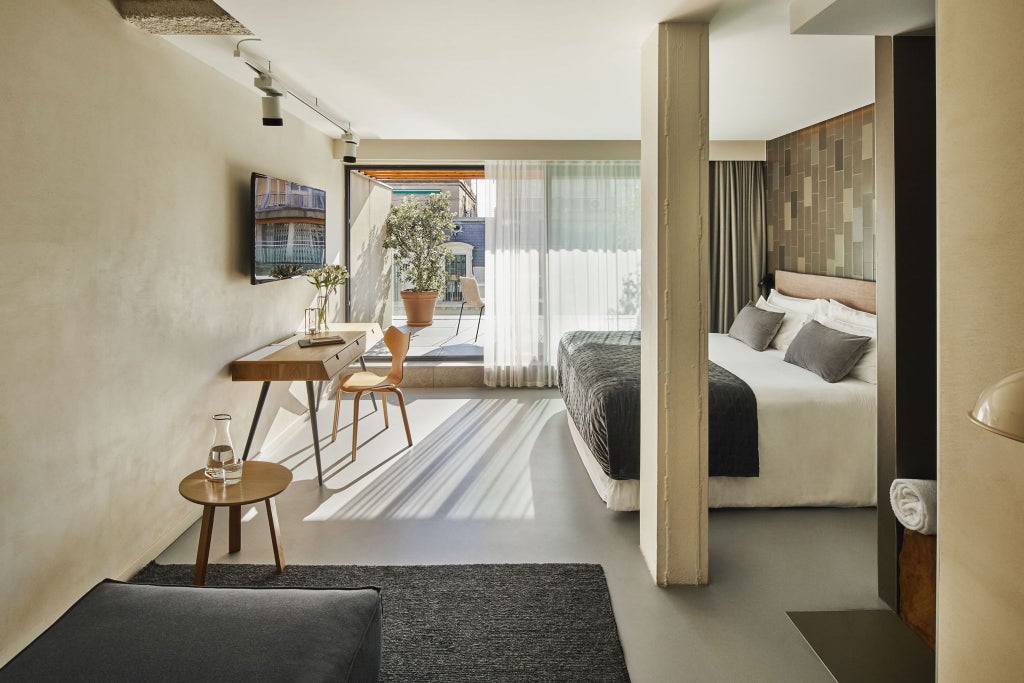 Modern luxury hotel room with elegant gray and white decor, king-sized bed, minimalist design, large window with city view at Ohla Eixample in Barcelona, Spain