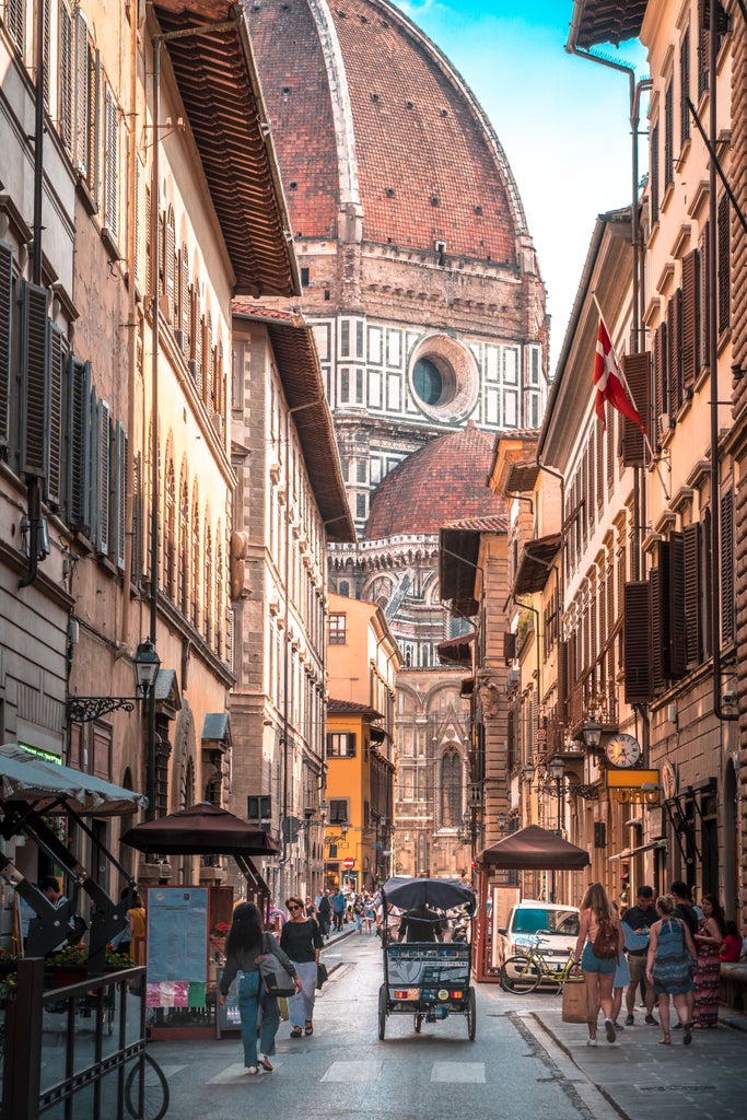 Historical Florence cityscape at dusk, featuring illuminated Duomo cathedral and Bell Tower against warm pink-orange sky, terracotta rooftops below