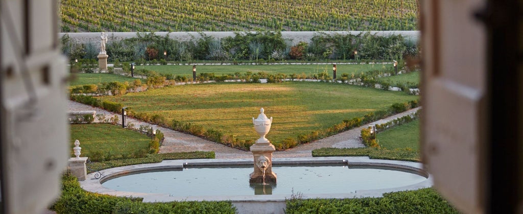 Elegant 18th-century French château with manicured gardens, stone facade, and symmetrical windows set against lush Provençal landscape at golden hour