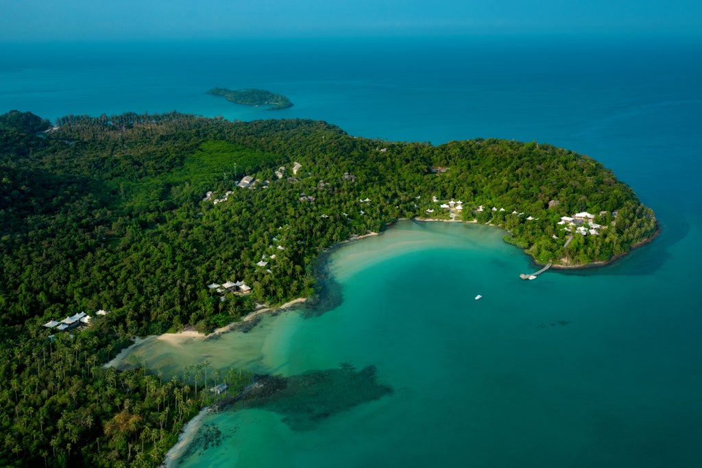 Luxurious overwater villa with glass floor panels at Soneva Kiri resort, surrounded by turquoise Thai waters and lush tropical forest