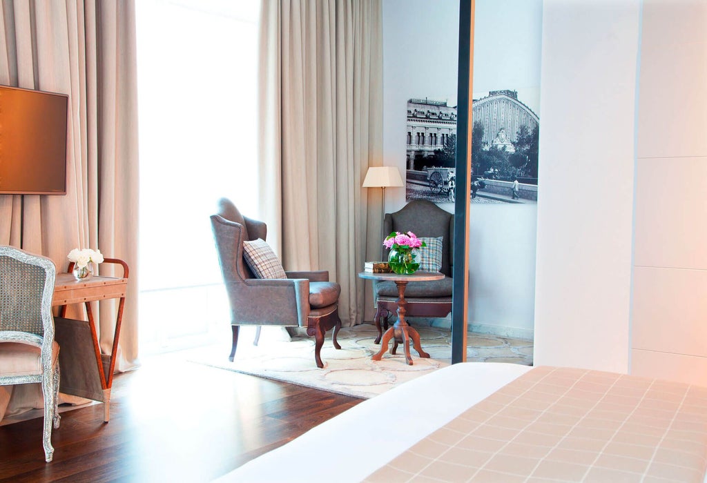 Elegant junior suite at URSO Hotel & Spa, Madrid, featuring plush white bedding, classic wooden furnishings, and sophisticated city palace view through expansive windows