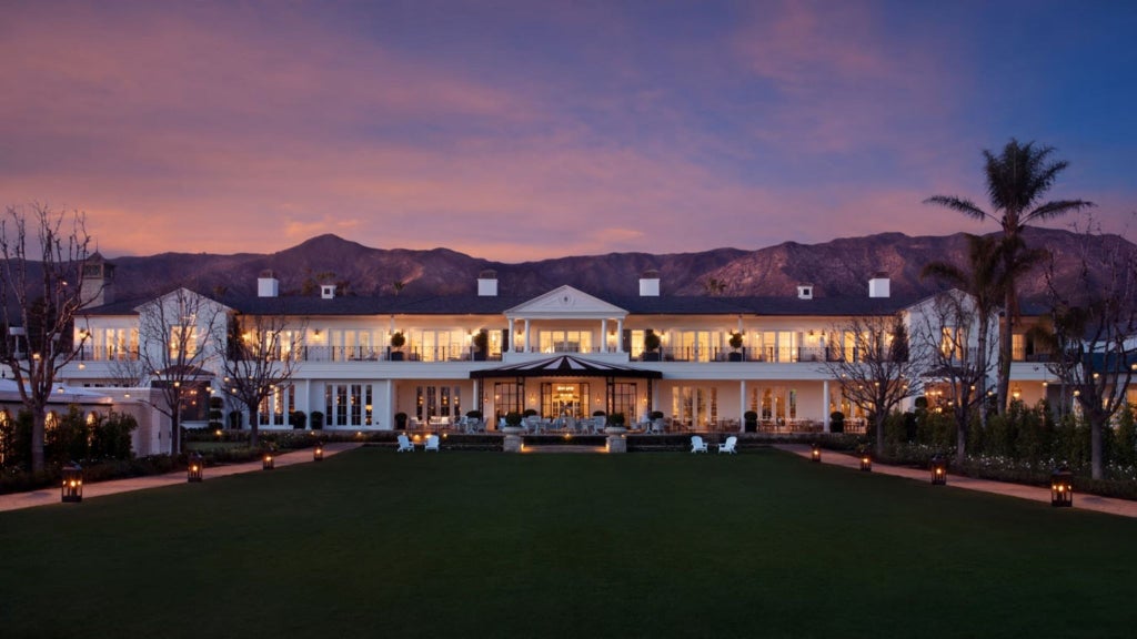 Luxurious oceanfront resort with white beach loungers, palm trees, and elegant blue-tiled pool overlooking pristine Miramar Beach coastline