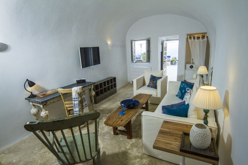 Luxurious whitewashed Cycladic suite with curved archways, blue-domed ceiling, private balcony overlooking Aegean Sea in Santorini's iconic cave hotel