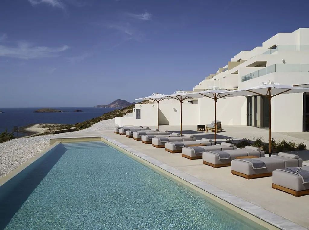 Luxurious white villa with private infinity pool overlooking the Aegean Sea, nestled into Milos' rugged coastal cliffside at sunset