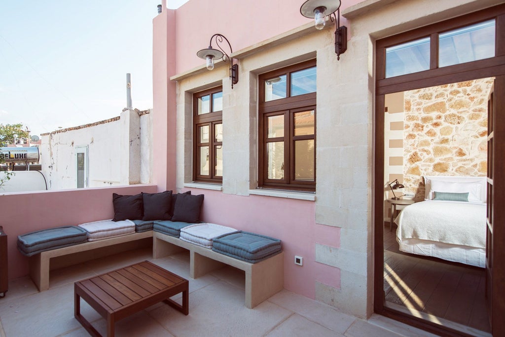 Elegant marble-floored suite with white furnishings, plush bedding, and a sun-drenched private terrace overlooking scenic Greek coastal landscape