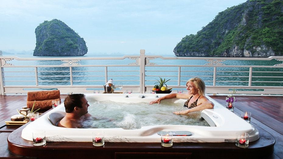 Luxurious white cruise ship sailing through emerald waters of Halong Bay, showcasing elegant decks and traditional Vietnamese maritime design against limestone karsts