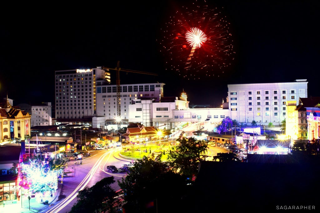 Night skyline of Phnom Penh with illuminated Royal Palace, elegant street lamps, and bustling riverside promenade showcasing Cambodia's vibrant urban sophistication.