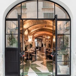 Elegant boutique hotel facade in Palma, Spain, with white colonial-style architecture, lush tropical plants, and sophisticated architectural details at dusk