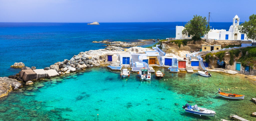 Traditional whitewashed Greek buildings cascade down rocky cliffs overlooking crystal blue Aegean waters at sunset in Milos island