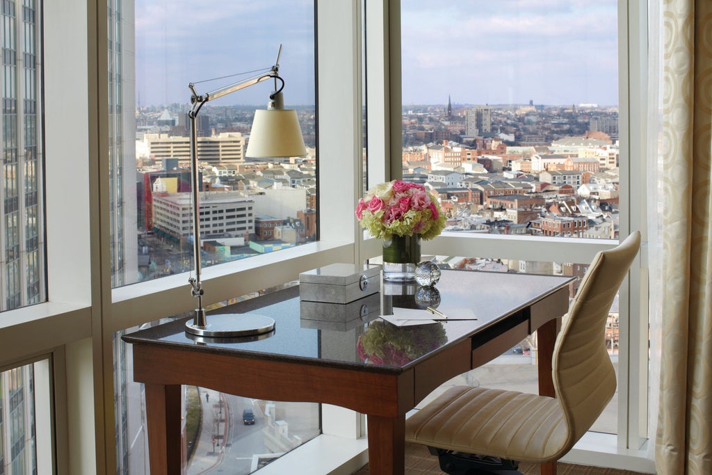 Modern glass skyscraper hotel overlooking Baltimore Harbor, featuring curved architecture, waterfront terrace and luxury pool deck at sunset