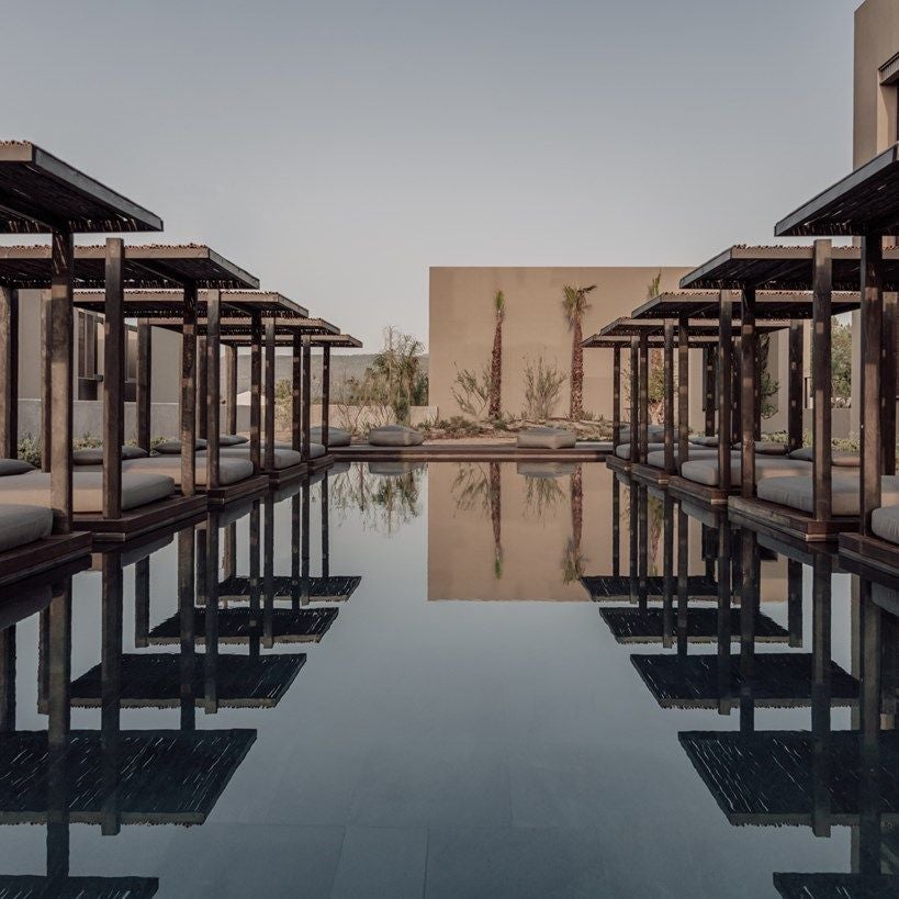 Sleek modern resort with white stone buildings nestled into mountainside, featuring infinity pool and bohemian-chic lounge areas