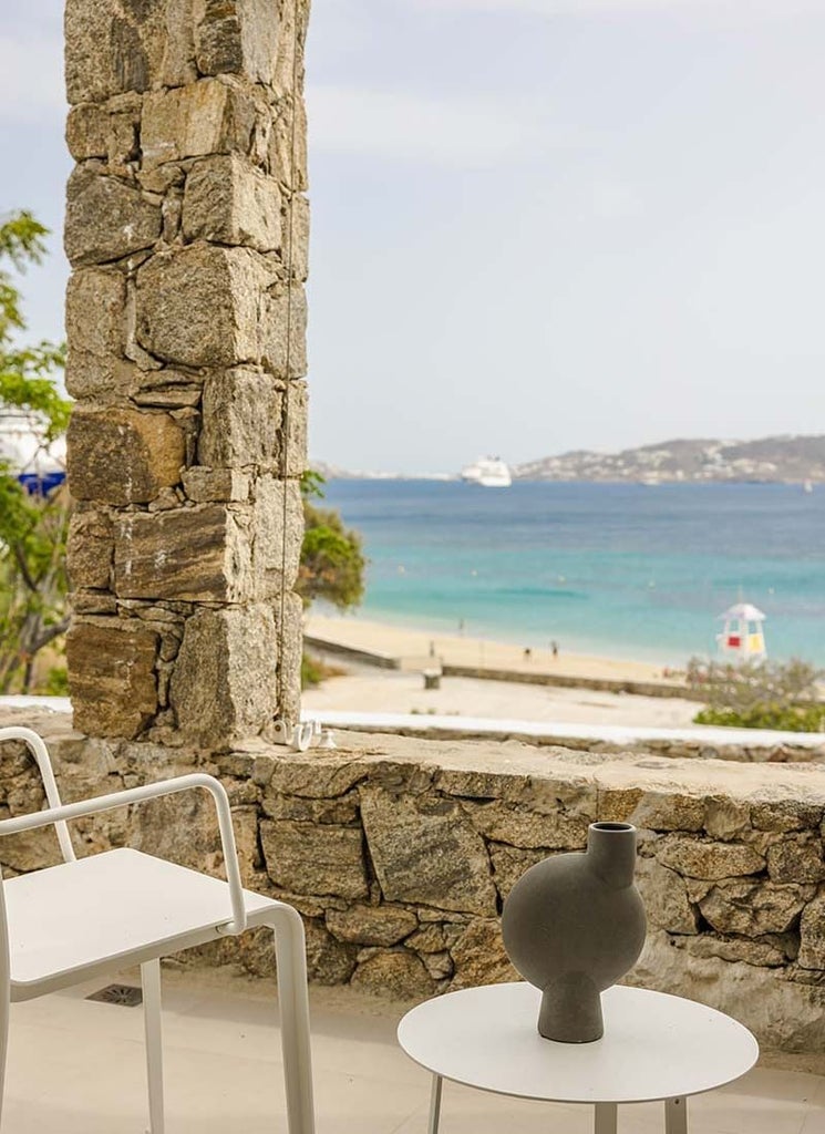 Luxurious white-themed superior suite with expansive Aegean Sea view, minimalist design, king bed, and elegant modern Cycladic architectural elements in Mykonos