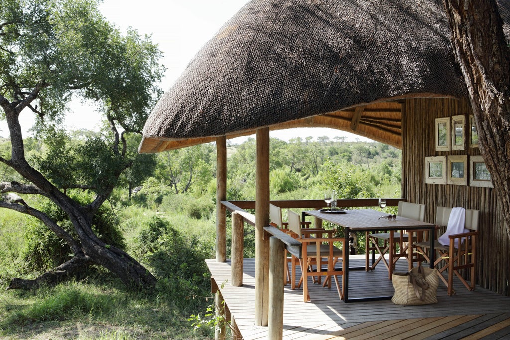 Luxurious safari lodge with thatched-roof suites overlooking private deck and infinity pool surrounded by African bushveld