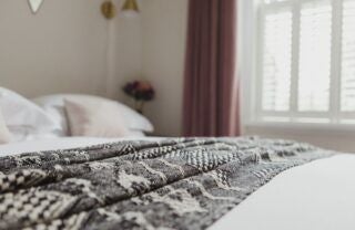 Elegant coastal-inspired bedroom with crisp white linens, plush throw pillows, and panoramic sea view through large windows at luxury seaside accommodation